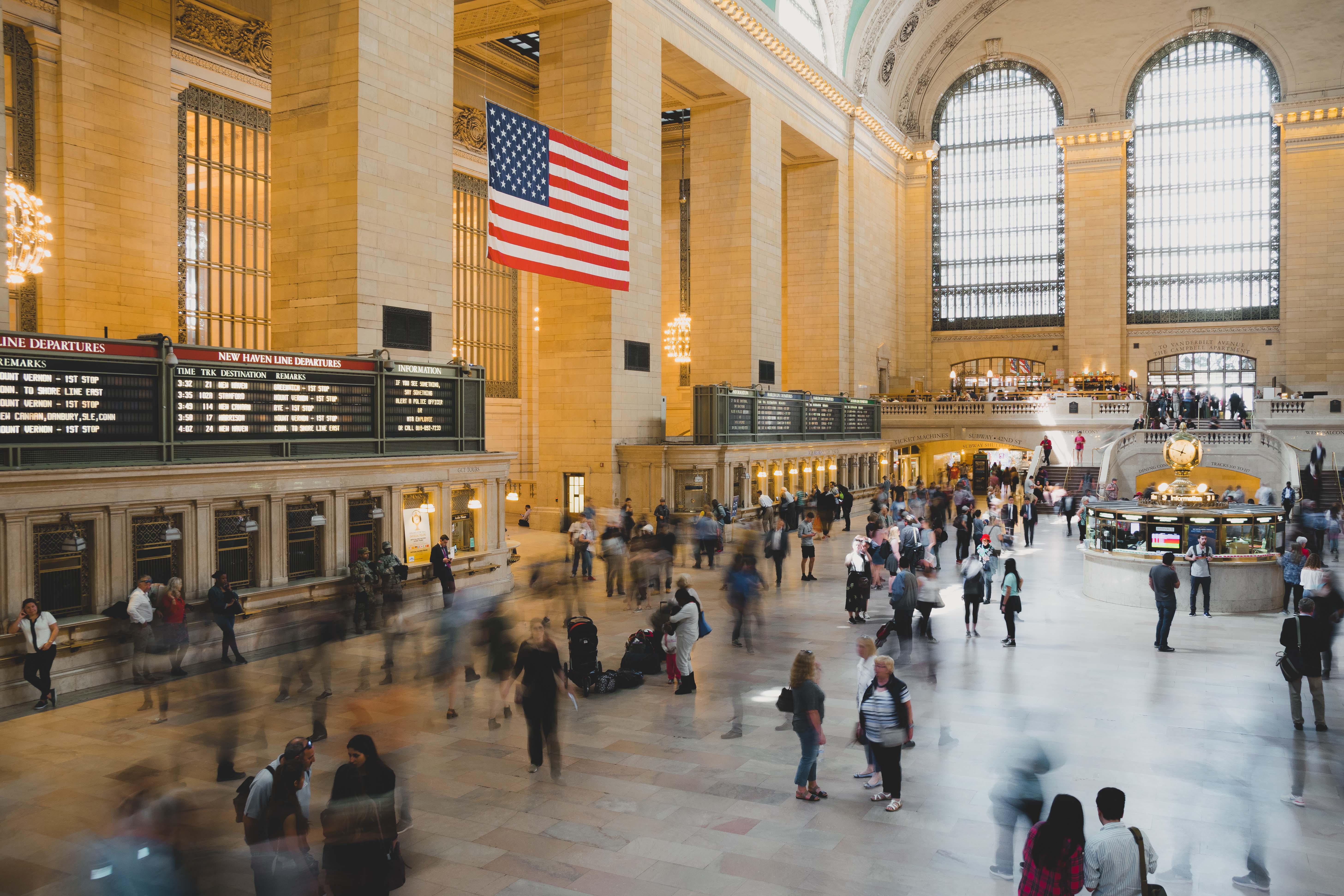 View of main hall in Grand Central long exposure with people moving quickly below the American flag and large windows