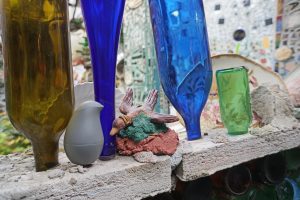 Birdie with bird statue friend amonst colorful upside down bottles blue and green in the mosaic wall