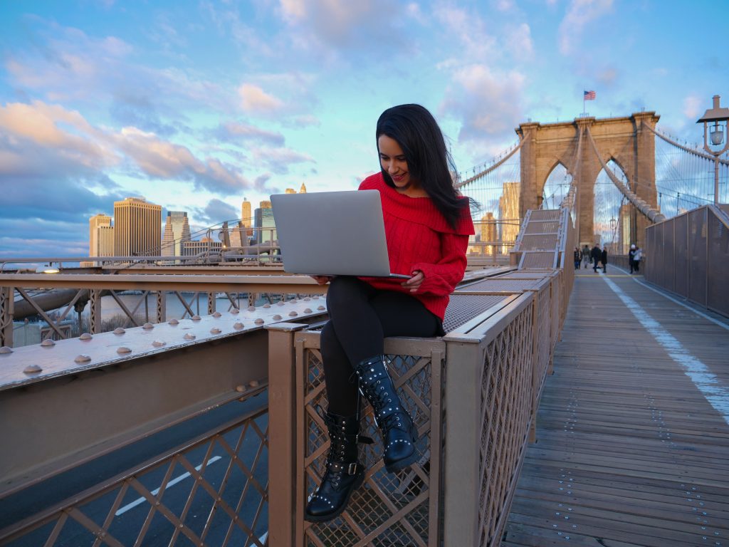 브루클린 다리 NYC 노트북 컴퓨터 비디오 편집에 빨간색 옷을 입은 소녀